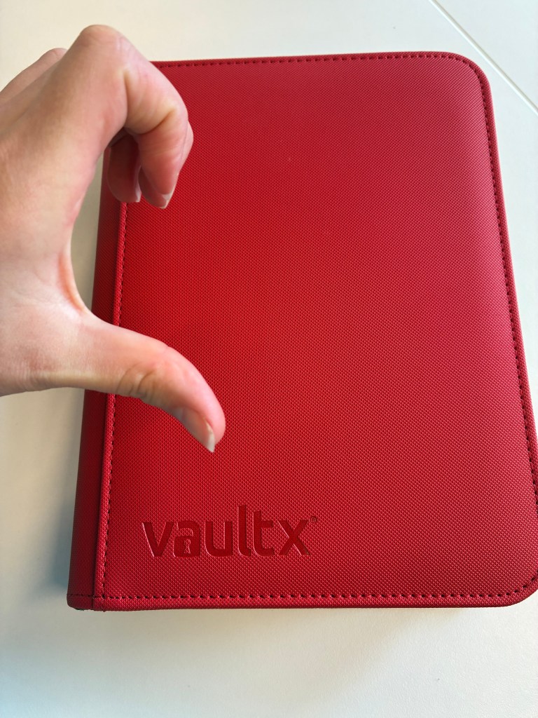 A hand making a heart shape with fingers around a red Exo-Tec® Zip Binder featuring the 'vaultx' logo.
