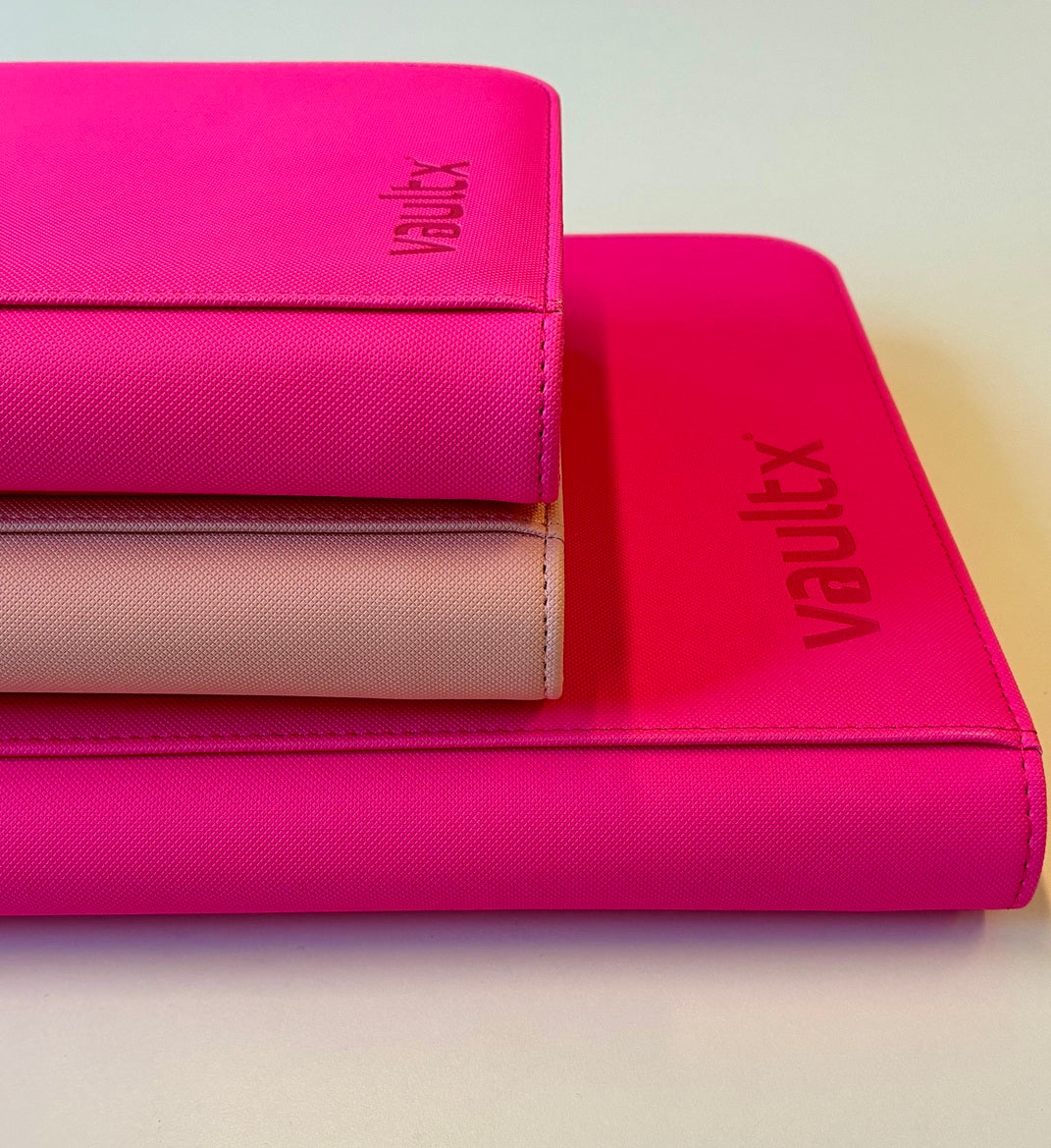 A stack of three colorful binders featuring 'Vault X' branding, with two shades of pink and a beige binder on the bottom.