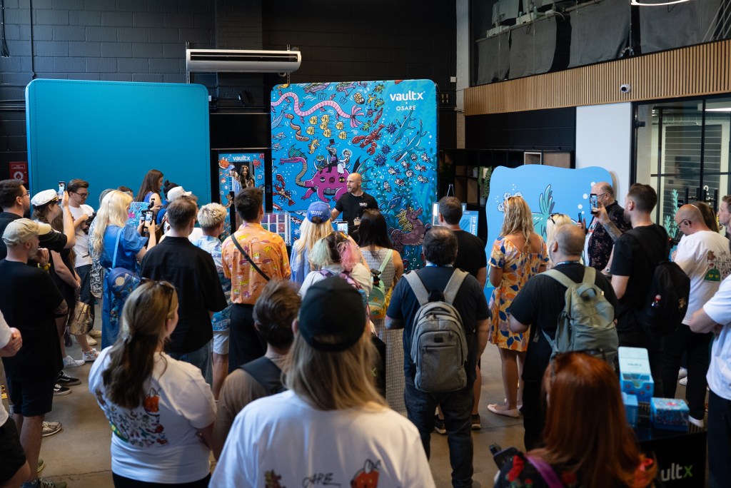 A crowd gathered at an event featuring a speaker in front of colorful backdrop displays with marine-themed artwork, showcasing an engaging atmosphere.